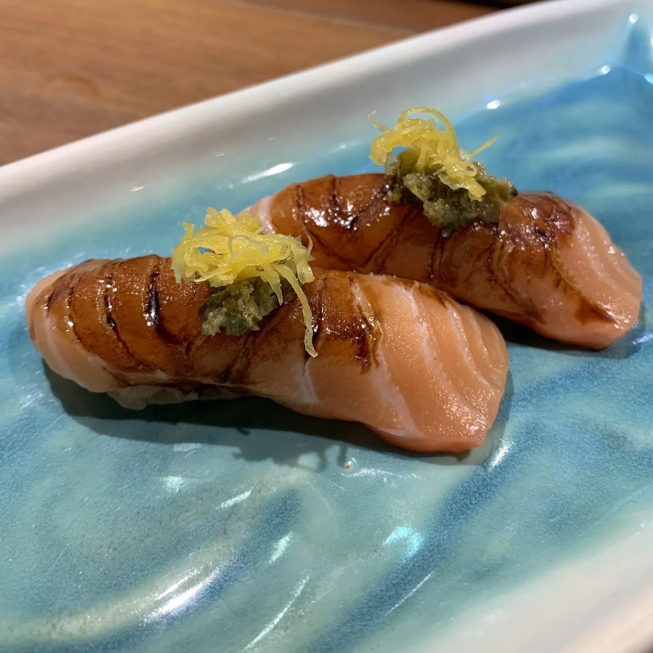 Two pieces of seared salmon nigiri topped with zest on a blue plate