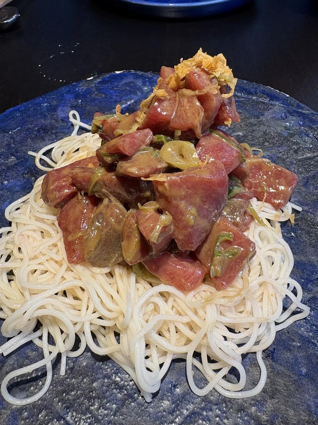 A pile of tuna tartare served over a nest of thin noodles on a blue plate