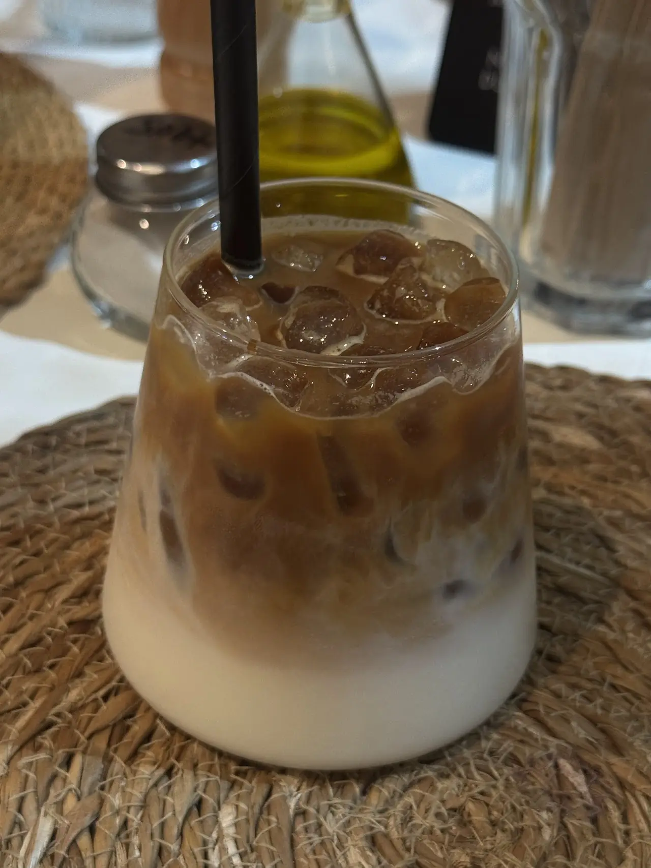 An iced latte with visible coffee-milk layers, served in a glass with a straw.