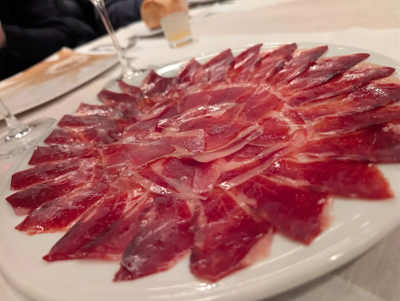 Thinly sliced cured ham fanned out on a round white plate.