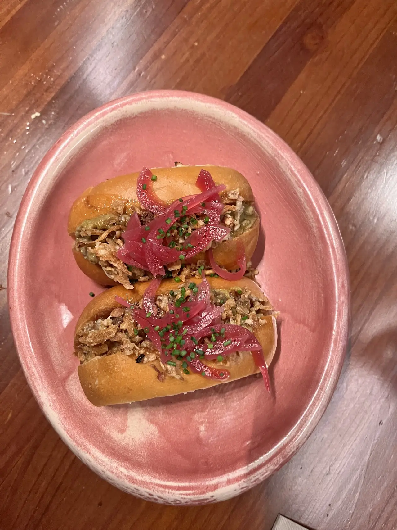 Two open-faced toasts topped with pickled red onion on a pink plate.