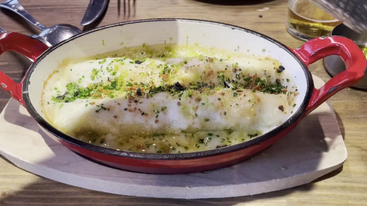 Rolled fish fillets in a green herb butter sauce inside a red enameled casserole dish.