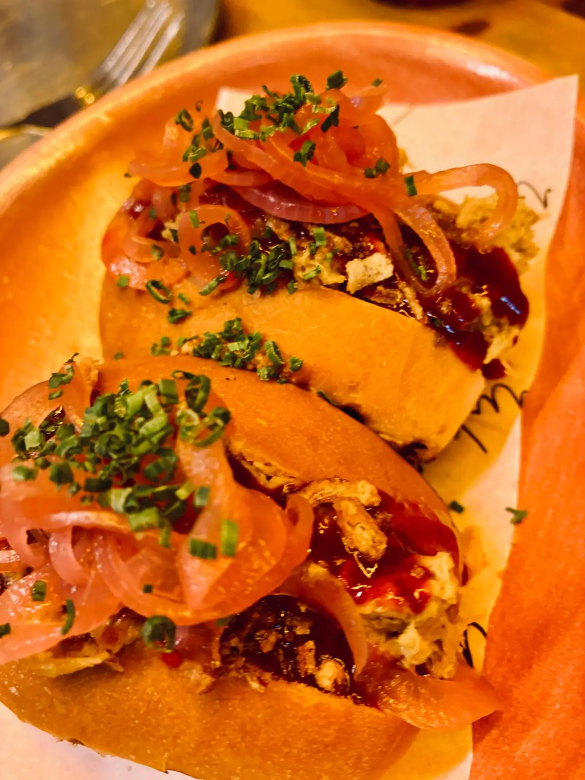 Two soft tacos topped with pickled red onion, crispy bits, and a drizzle of sauce.