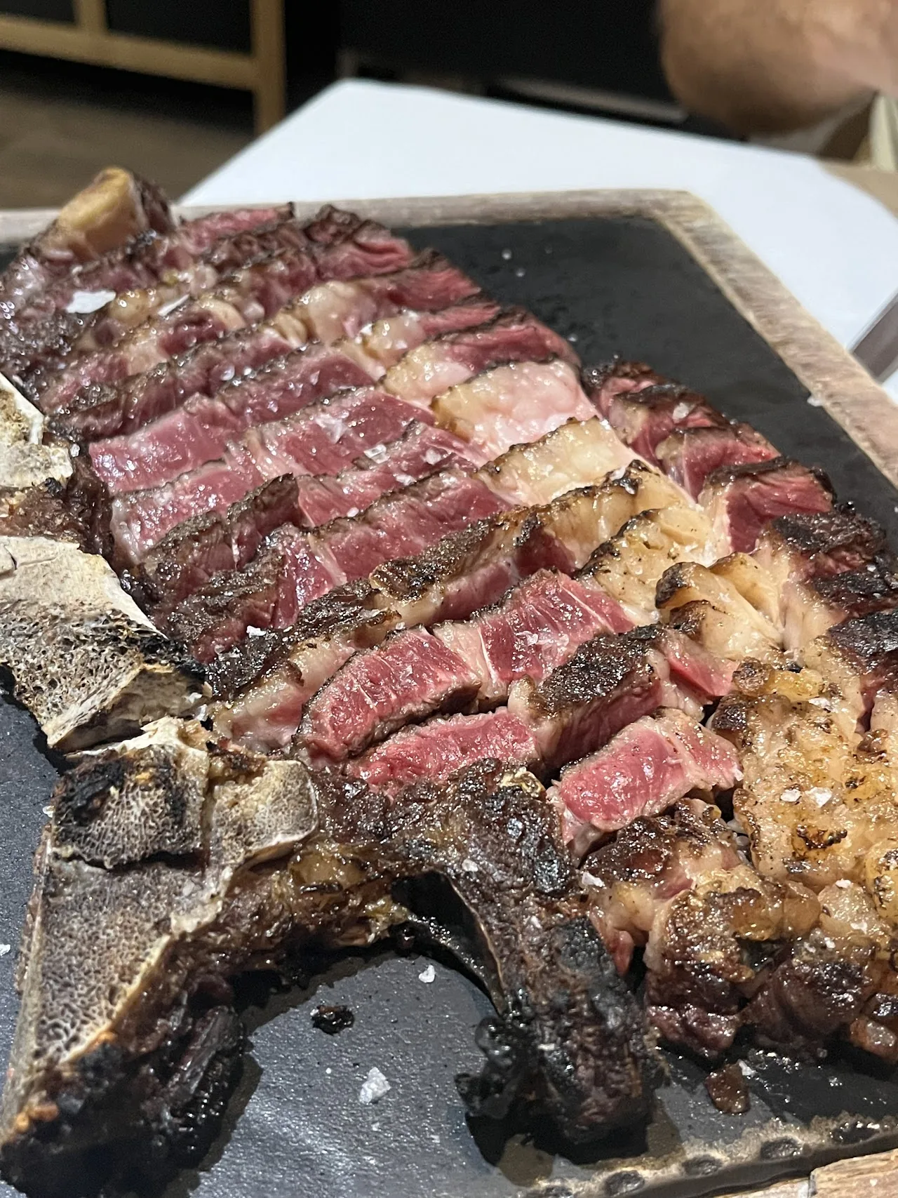 A sliced steak with a charred crust, seasoned with salt, on a board