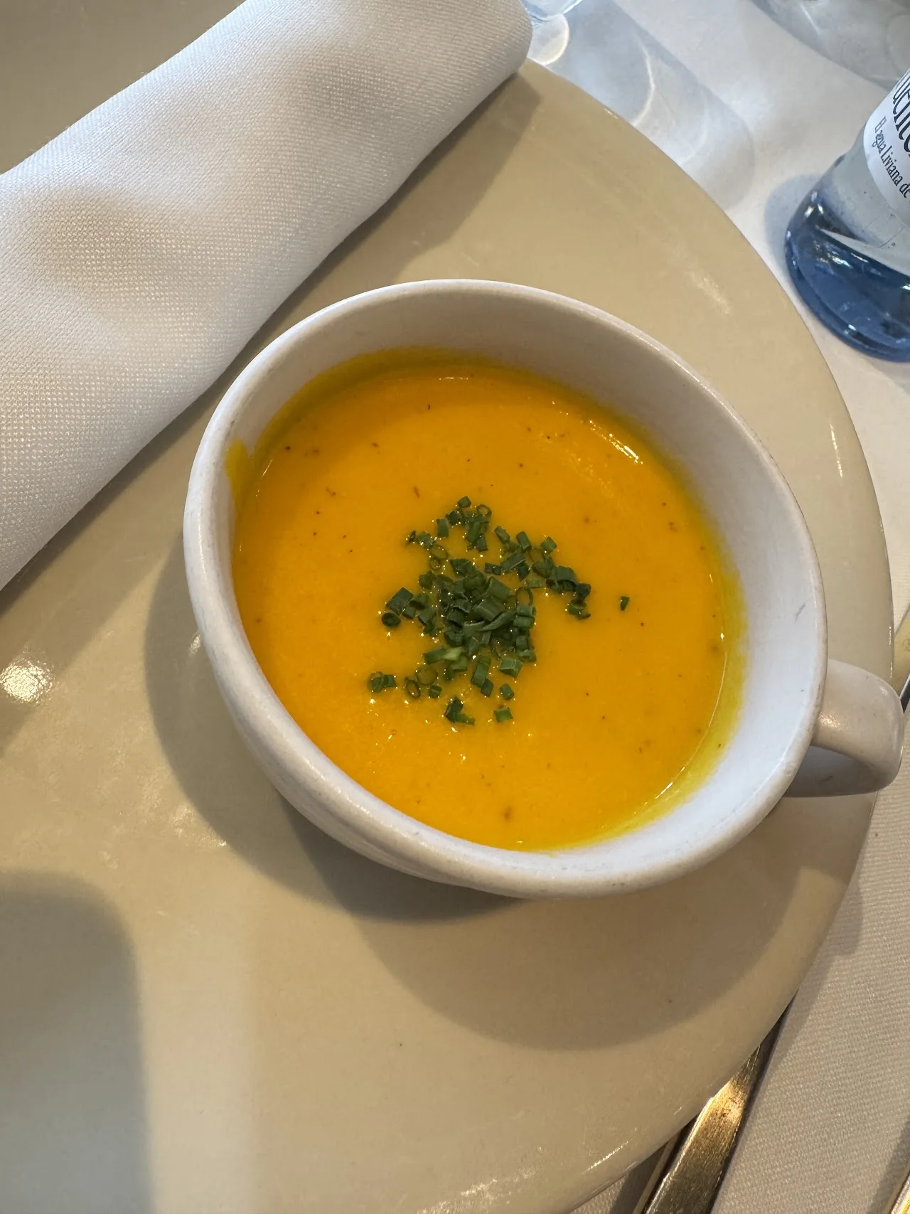 A cup of orange soup garnished with chives