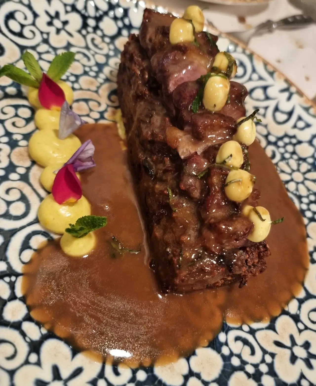 Sliced meat plated with a dark sauce and colorful garnish on a patterned dish.