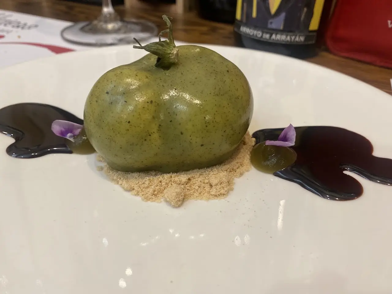 An apple-shaped green dessert on a white plate with a dark sauce swirl.