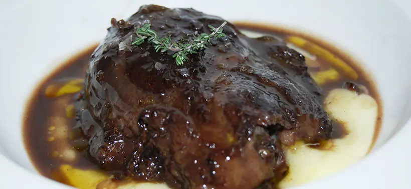 Braised meat in a dark reduction sauce with a sprig of thyme and mashed potato, at Valentin Restaurant Xarcuteria