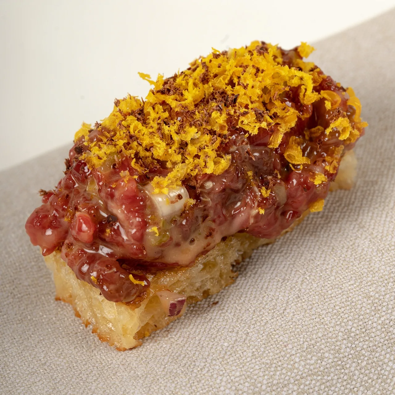 A rectangular piece of toasted bread topped with red minced meat and grated golden yolk
