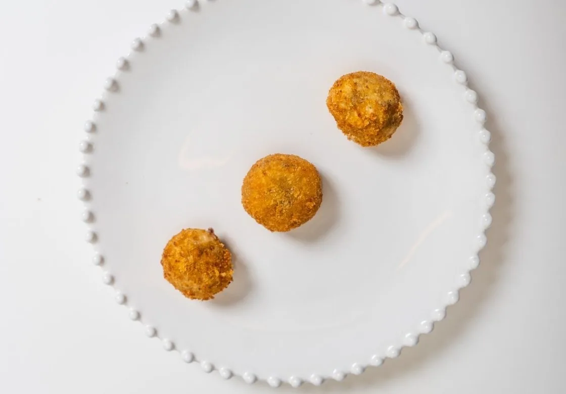 Three golden fried croquetas on a white beaded plate
