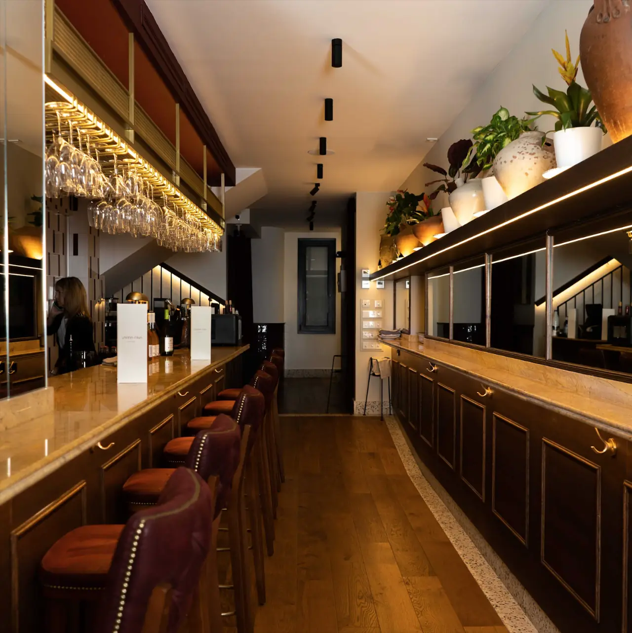 Restaurant bar area with a wooden counter, wine glasses on a shelf, and leather stools.