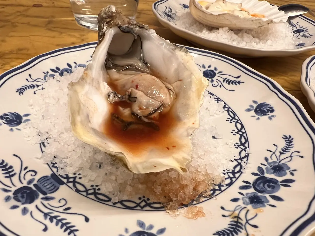 Oyster on the half shell with sauce, served over rock salt on a blue and white plate