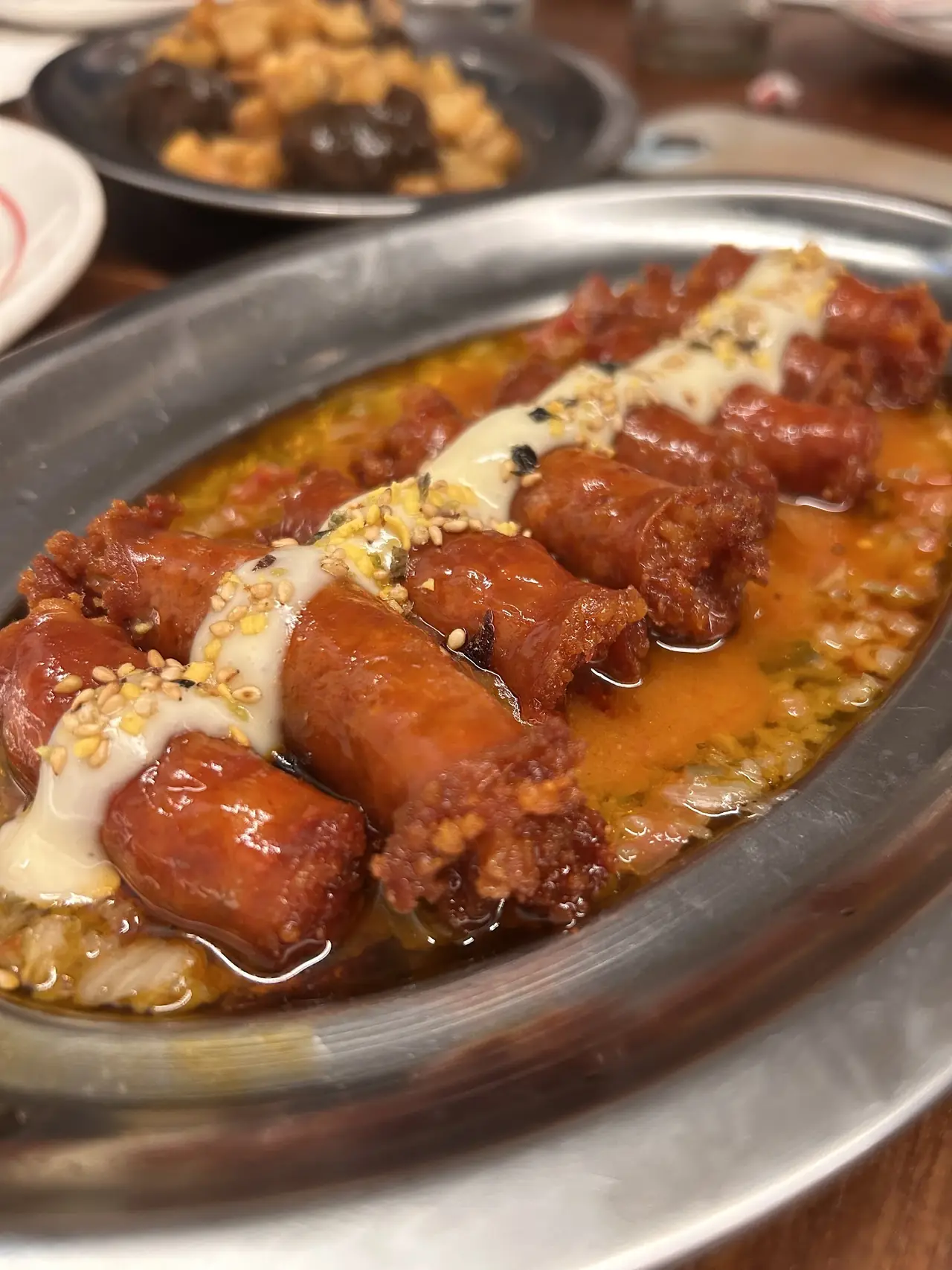 Small grilled sausages with a pale sauce on an oval metal platter