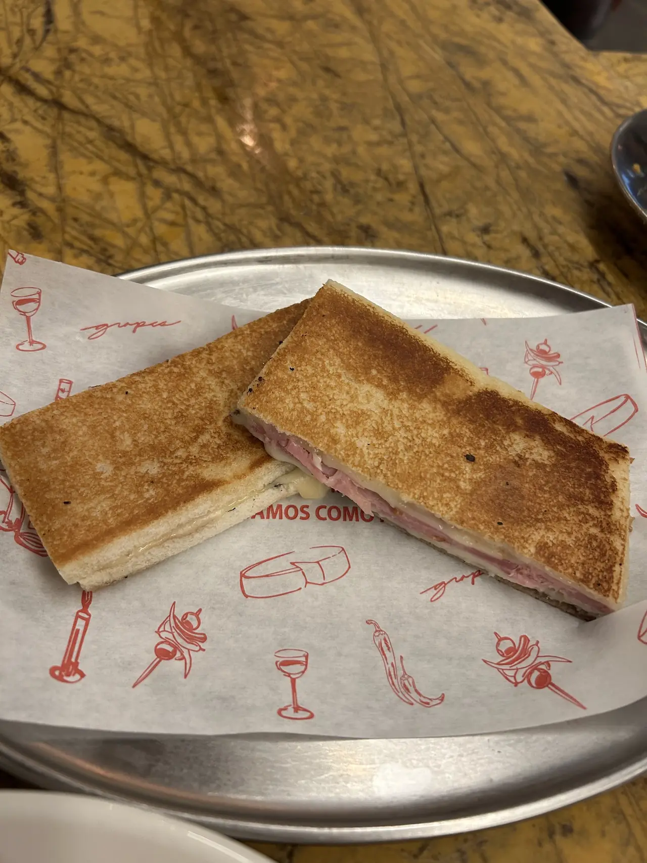 A toasted bikini sandwich cut in half on printed paper on a metal tray
