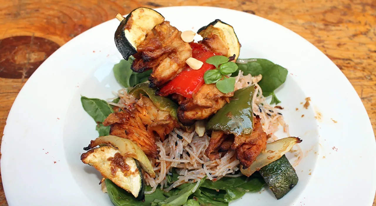 A white plate of grilled vegetables and sprouts on a bed of greens