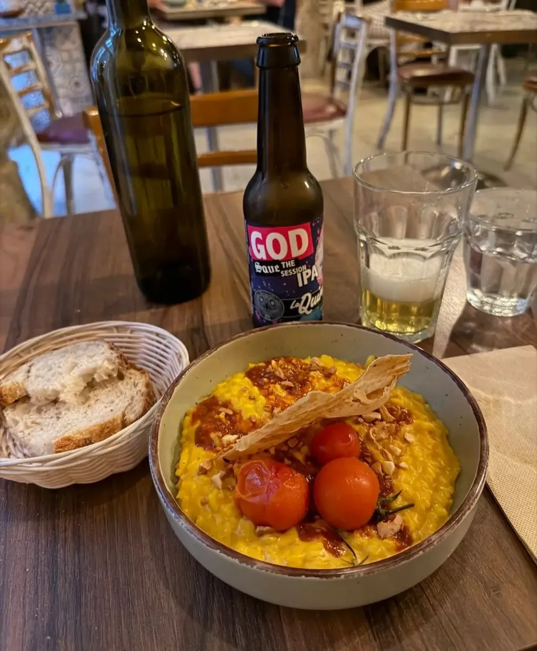 A shallow bowl of yellow rice with roasted tomatoes beside bread and a bottle