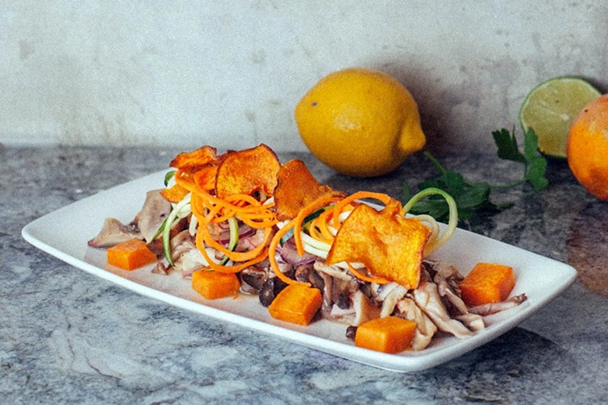 A white dish of shredded vegetables, orange squash cubes and mushroom pieces with a lemon beside it