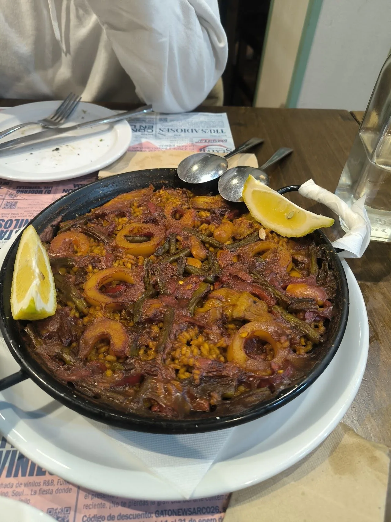 A black paella pan of rice with a lemon wedge