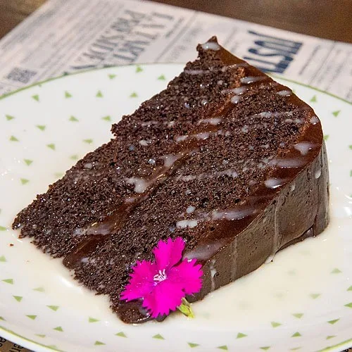 A slice of chocolate cake topped with a pink flower