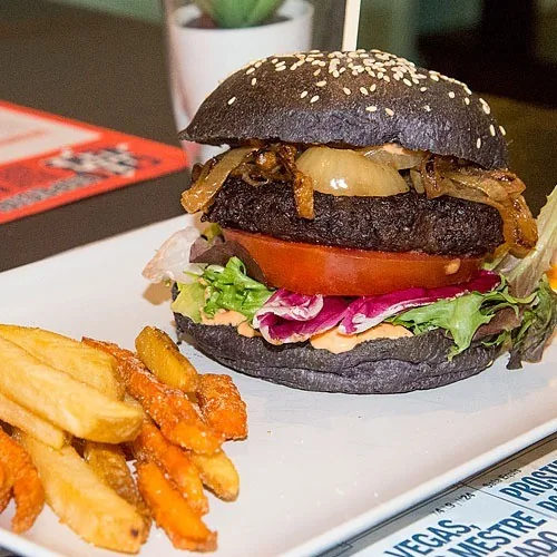 A black-bun burger with tomato, red cabbage and onions beside orange sweet potato fries