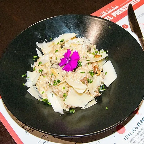 A black bowl of salad with shaved white slices and a purple flower on top