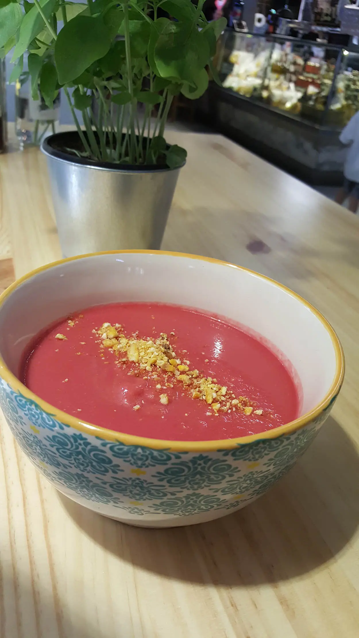 A bowl of pink cold soup (gazpacho-style) topped with crushed nuts, on a wooden table