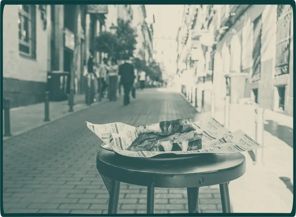 Steak sandwich wrapped in branded paper on a stool, street scene behind, duotone filter