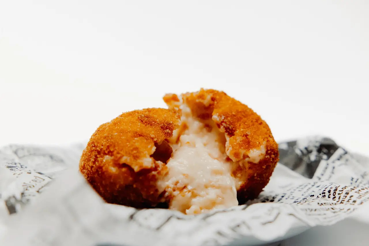 Fried croqueta split open showing creamy filling, served on newsprint paper