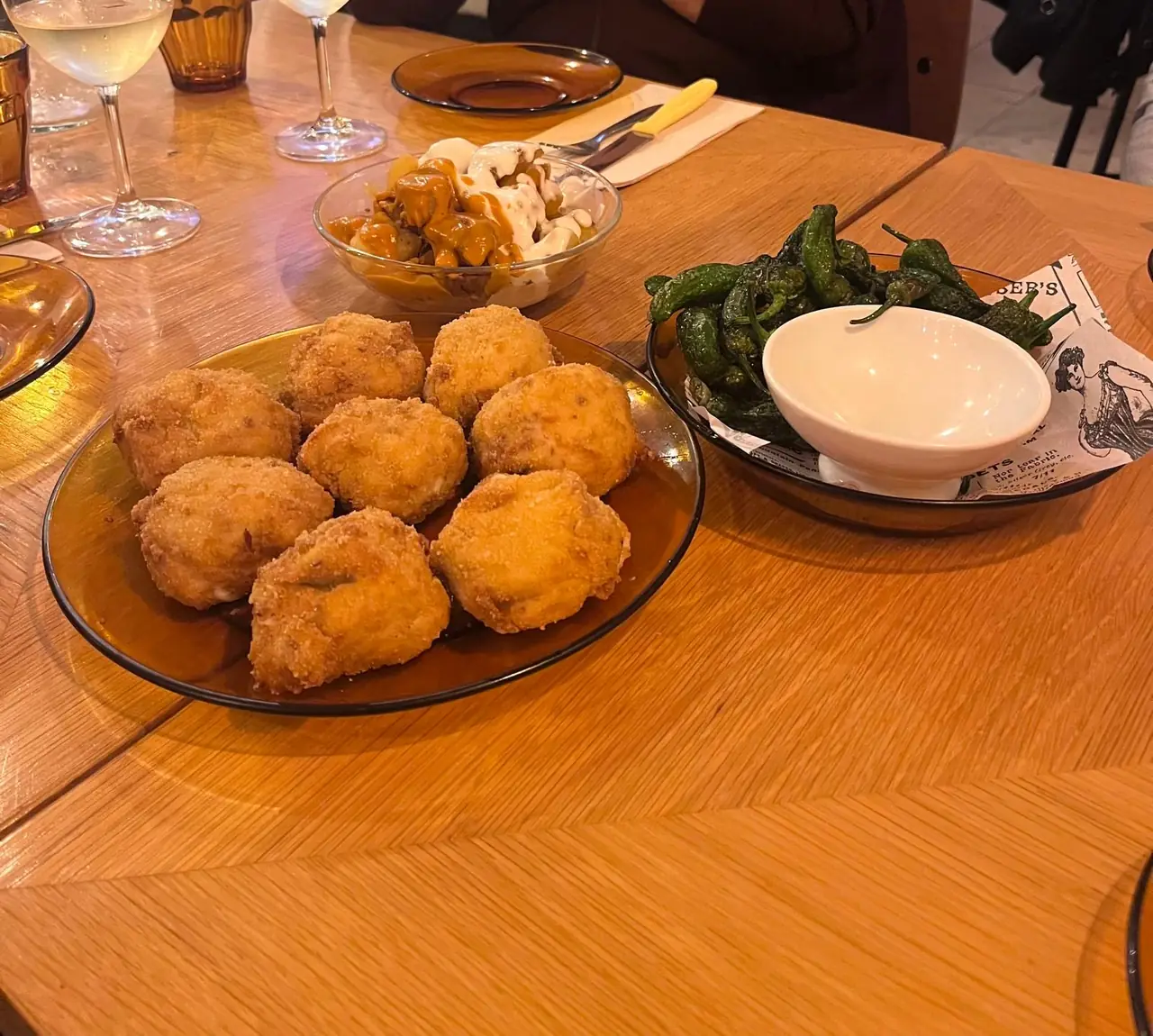 Croquetas, patatas bravas and fried padron peppers with aioli on wooden table