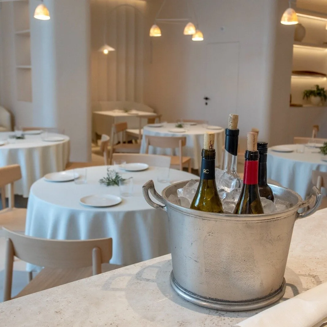 A dining room with round white-clothed tables and a metal bucket holding wine bottles