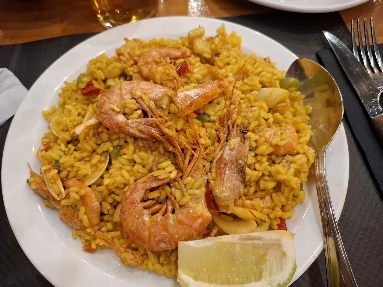 A plate of seafood paella with prawns and a lemon wedge