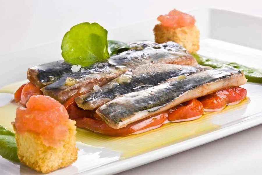 Grilled sardine fillets on a white plate with small tomato pieces
