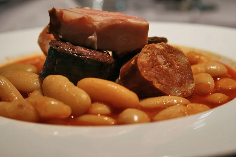 A white plate of white beans with pork and sausage