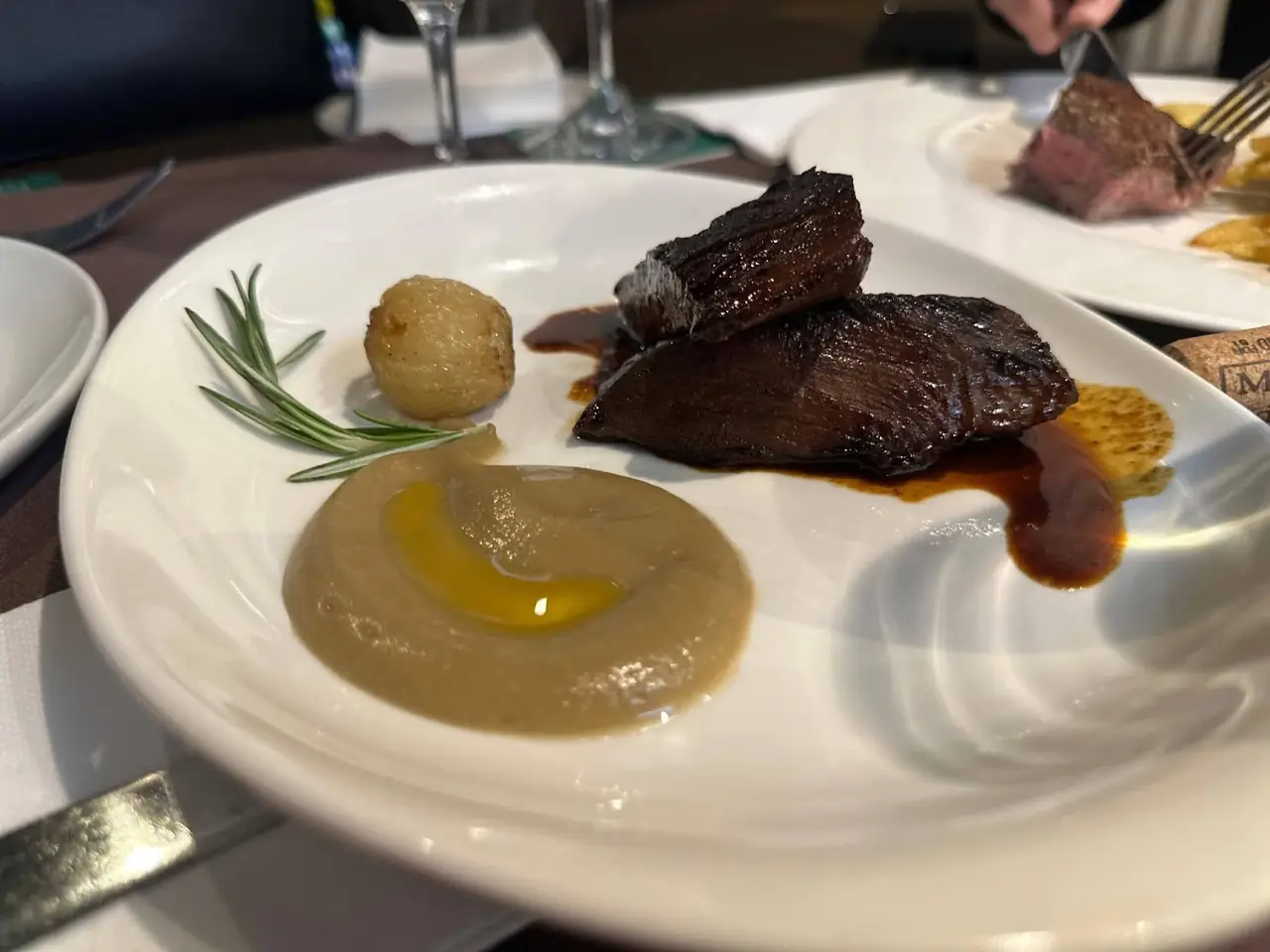 Braised beef with a jus, a puree, roasted onion and rosemary sprig on a plate