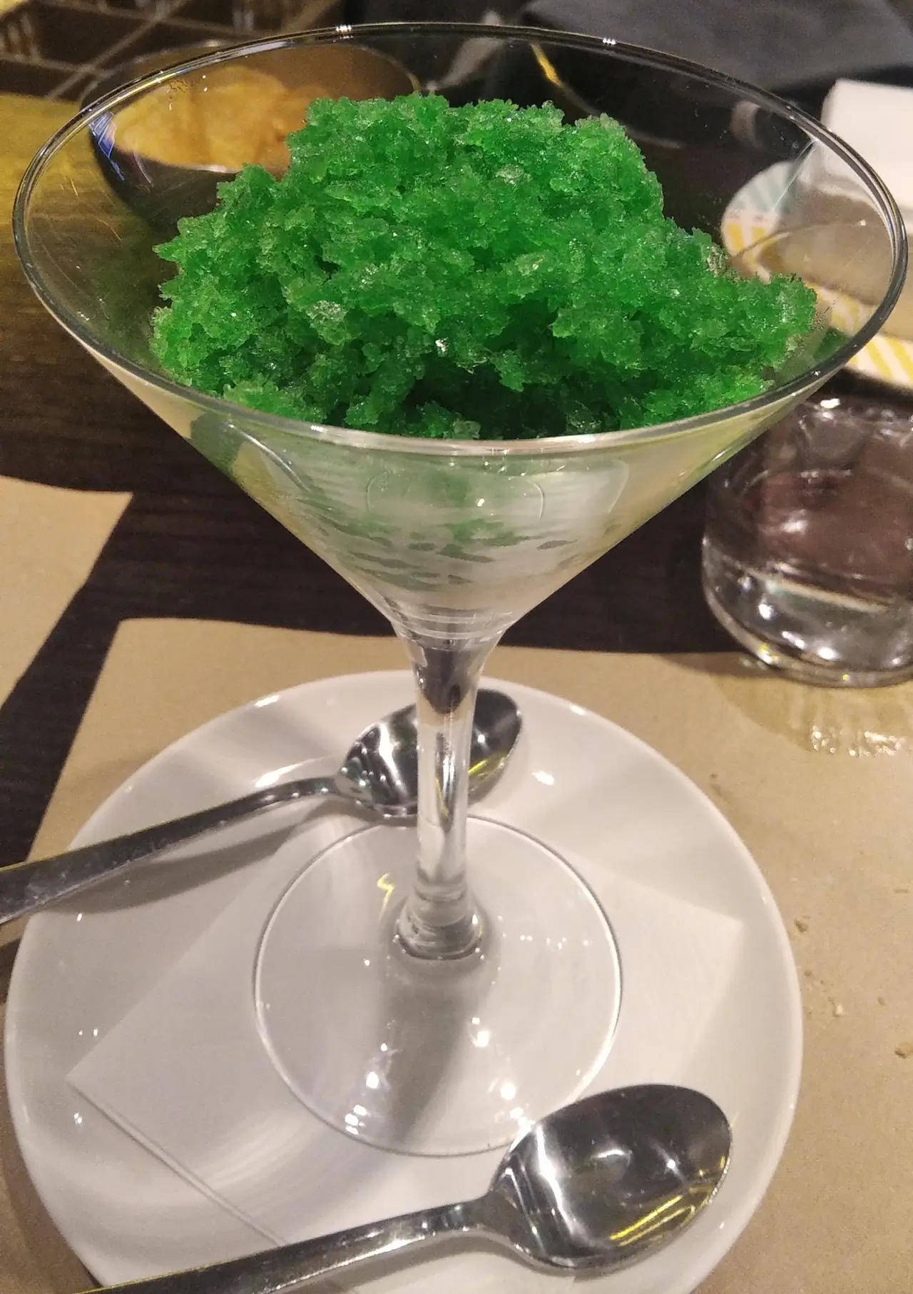 Green granita served in a martini glass on a saucer with spoons