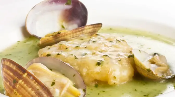 Fish fillet in green herb sauce with open clams in a white bowl