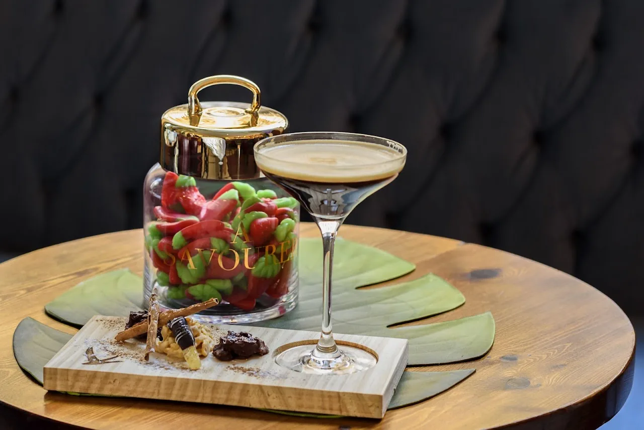 A martini cocktail with olives, served on a wooden board with snacks