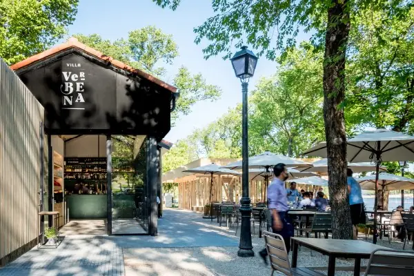 Exterior of Villa Verbena, a black gabled pavilion with white logo signage and a lakeside terrace of umbrella-shaded tables