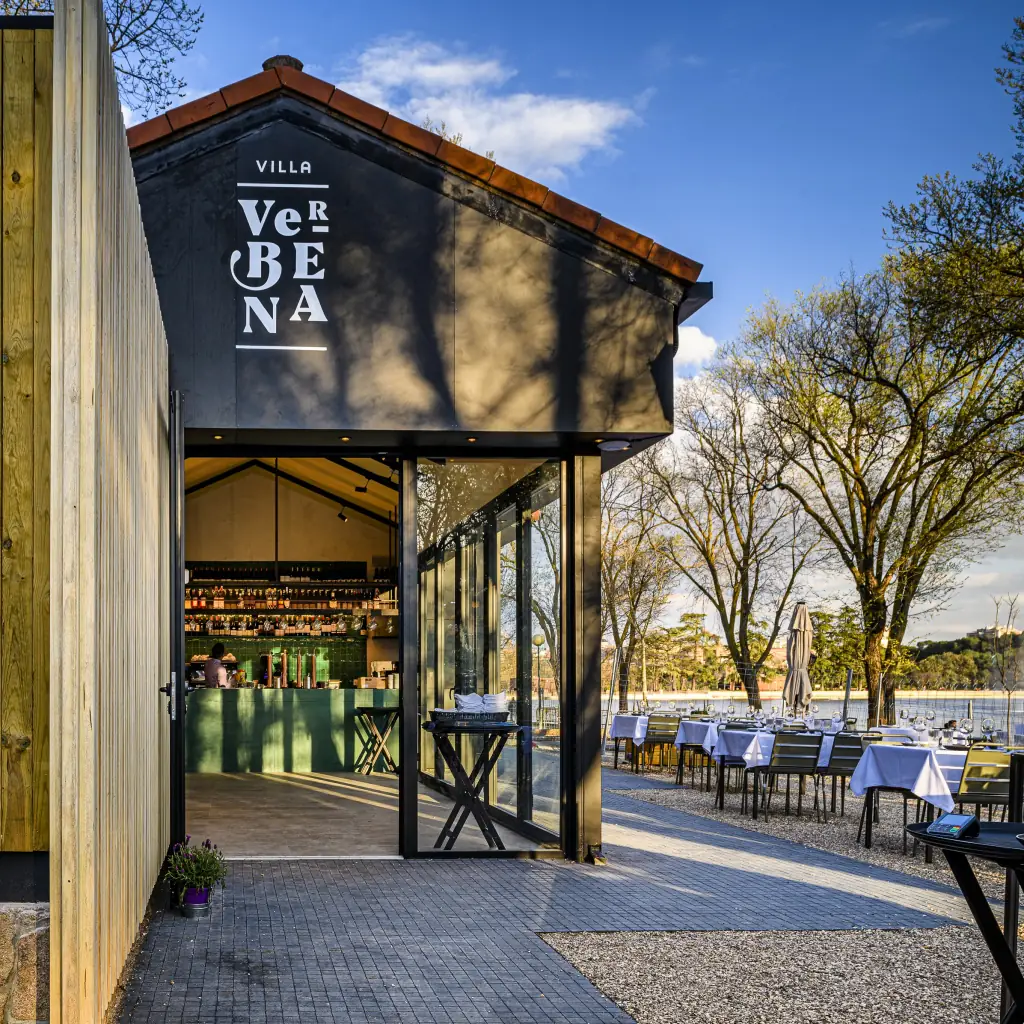 Entrance of Villa Verbena with green-tiled bar visible inside and white-linen terrace tables by the lake at dusk