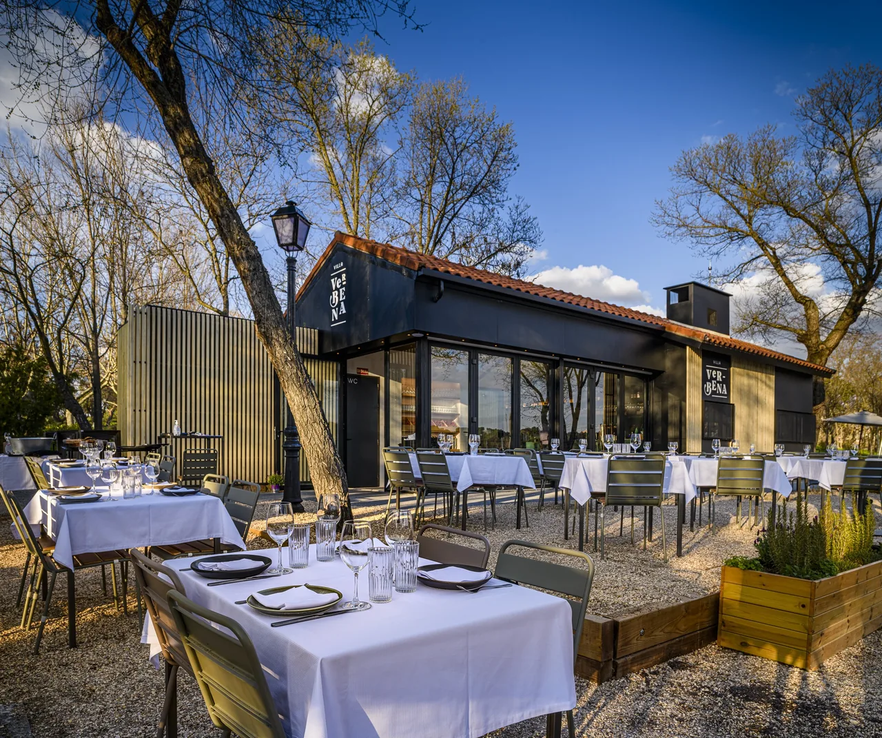 Set tables on a gravel terrace in front of a dark wooden building with a tiled roof