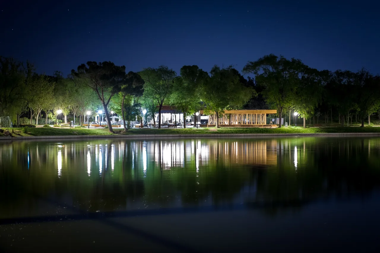 A lake at night with a lit pavilion and trees reflected in the water
