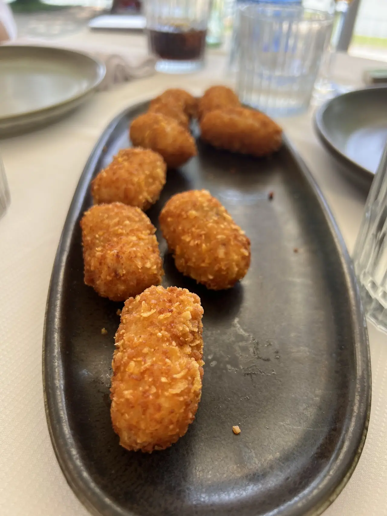 Breaded, fried croquettes lined up on a dark oval plate.