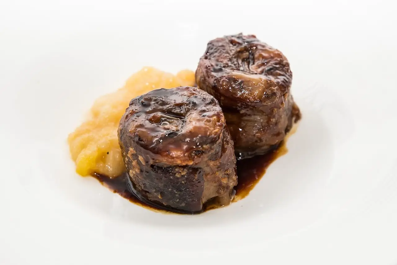 Two seared meat medallions in a dark sauce with an orange purée