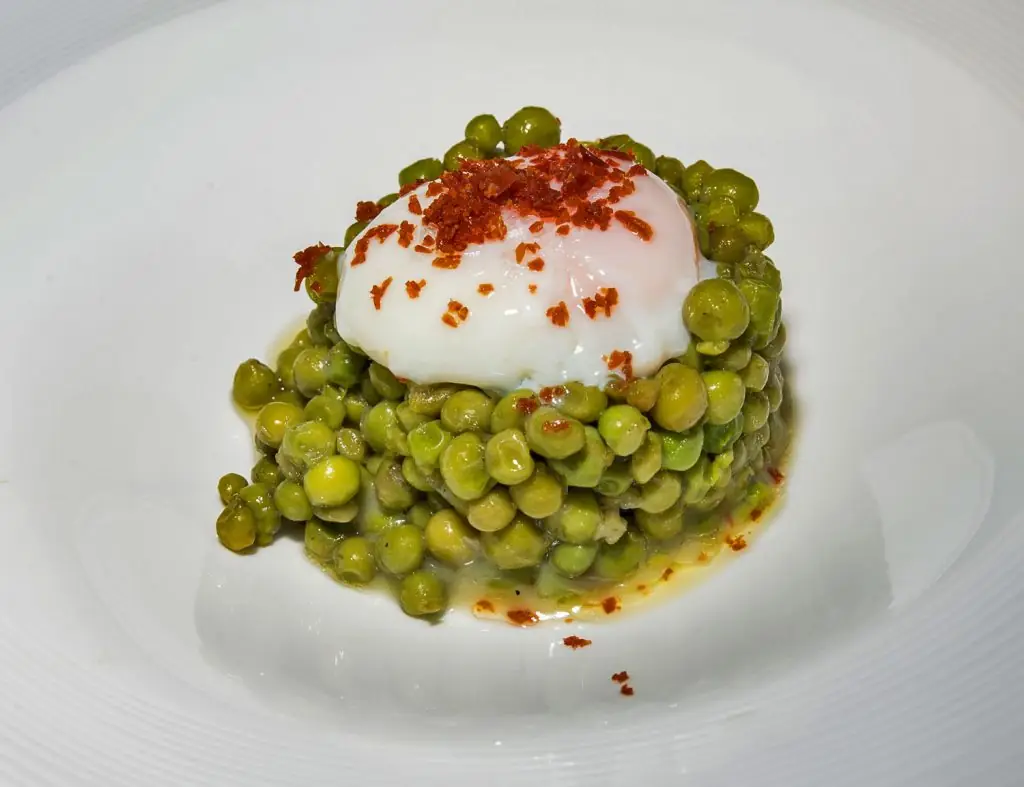 Mound of green peas topped with a poached egg and crispy jamon crumbs on a white plate