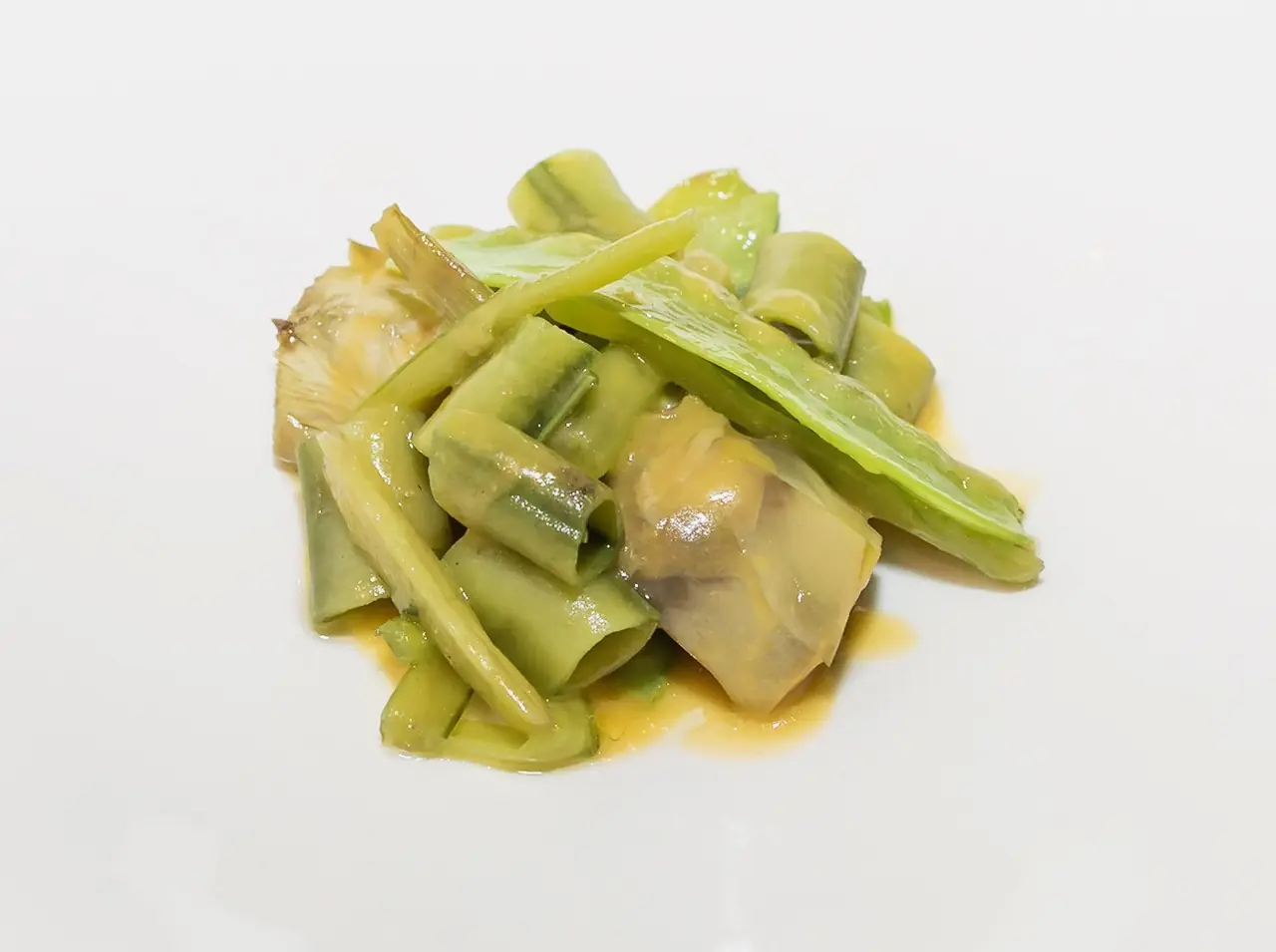 Sauteed green asparagus and artichoke pieces in light sauce on a white plate