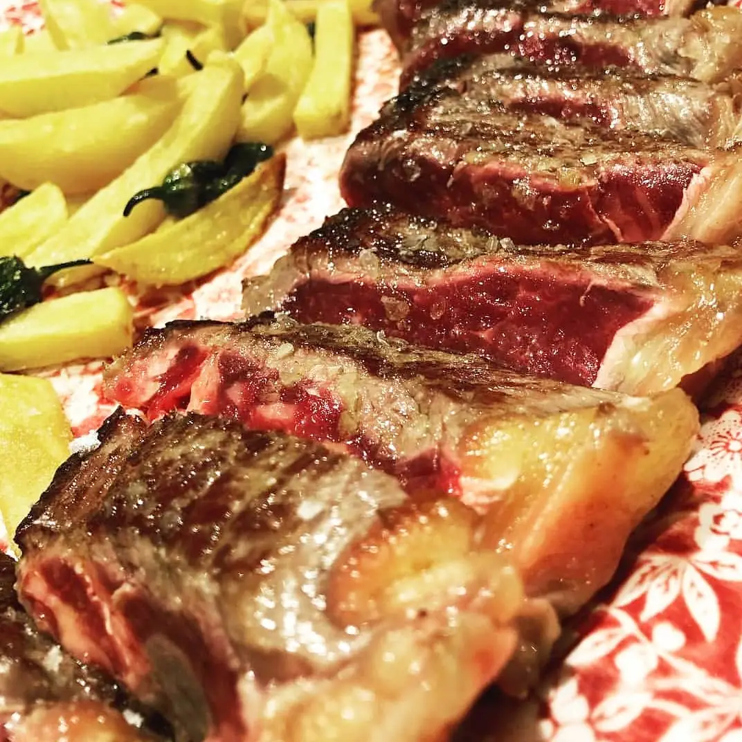 Close-up of sliced grilled beef steak with coarse salt, fried potatoes and padron peppers