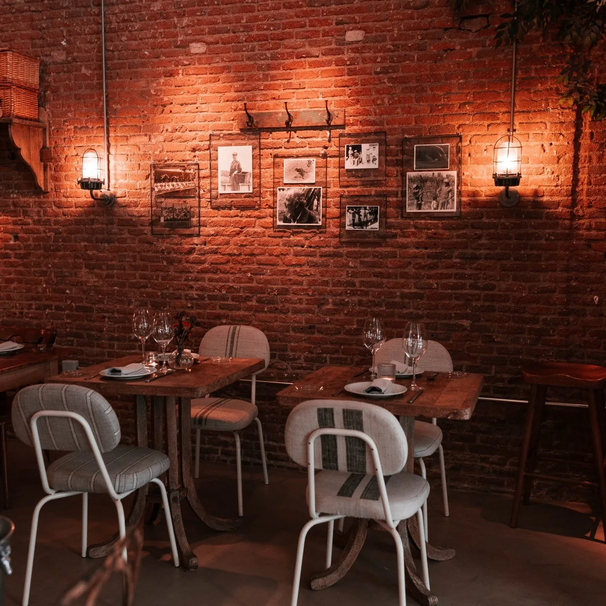 A brick-walled dining room with wooden tables, white chairs and framed photos