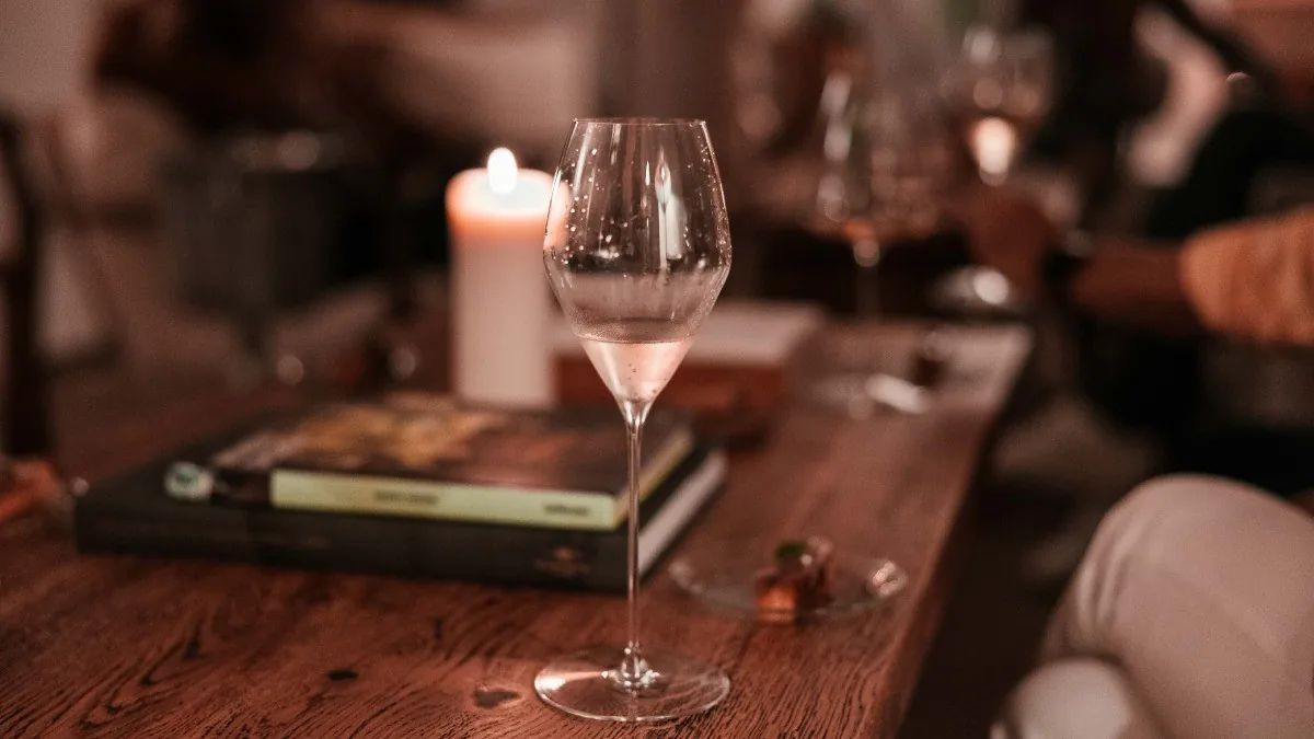 A wine glass on a wooden table with a lit candle and a book