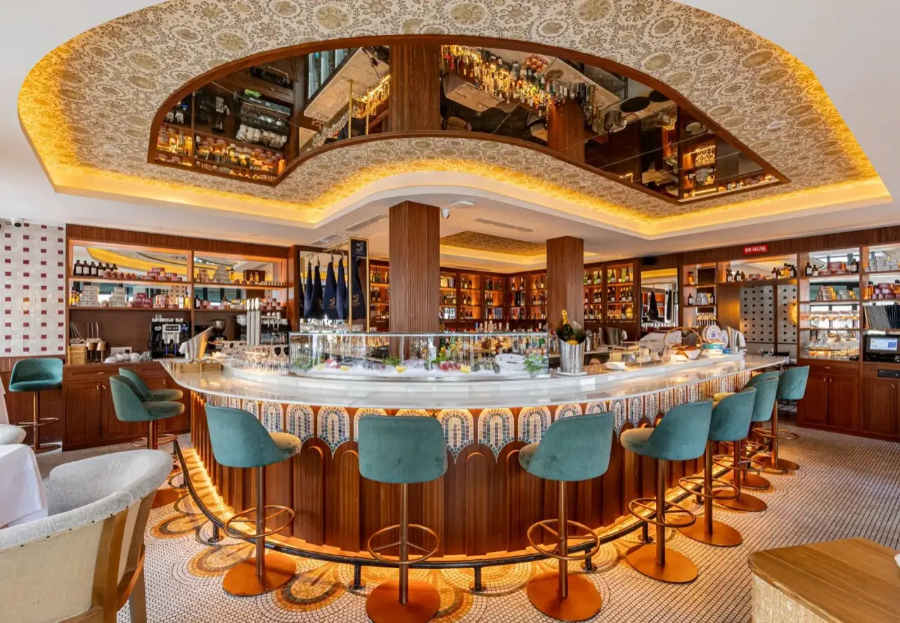 Ornate curved bar with teal velvet stools, a marble seafood-on-ice counter, mirrored overhead canopy and shelves of bottles