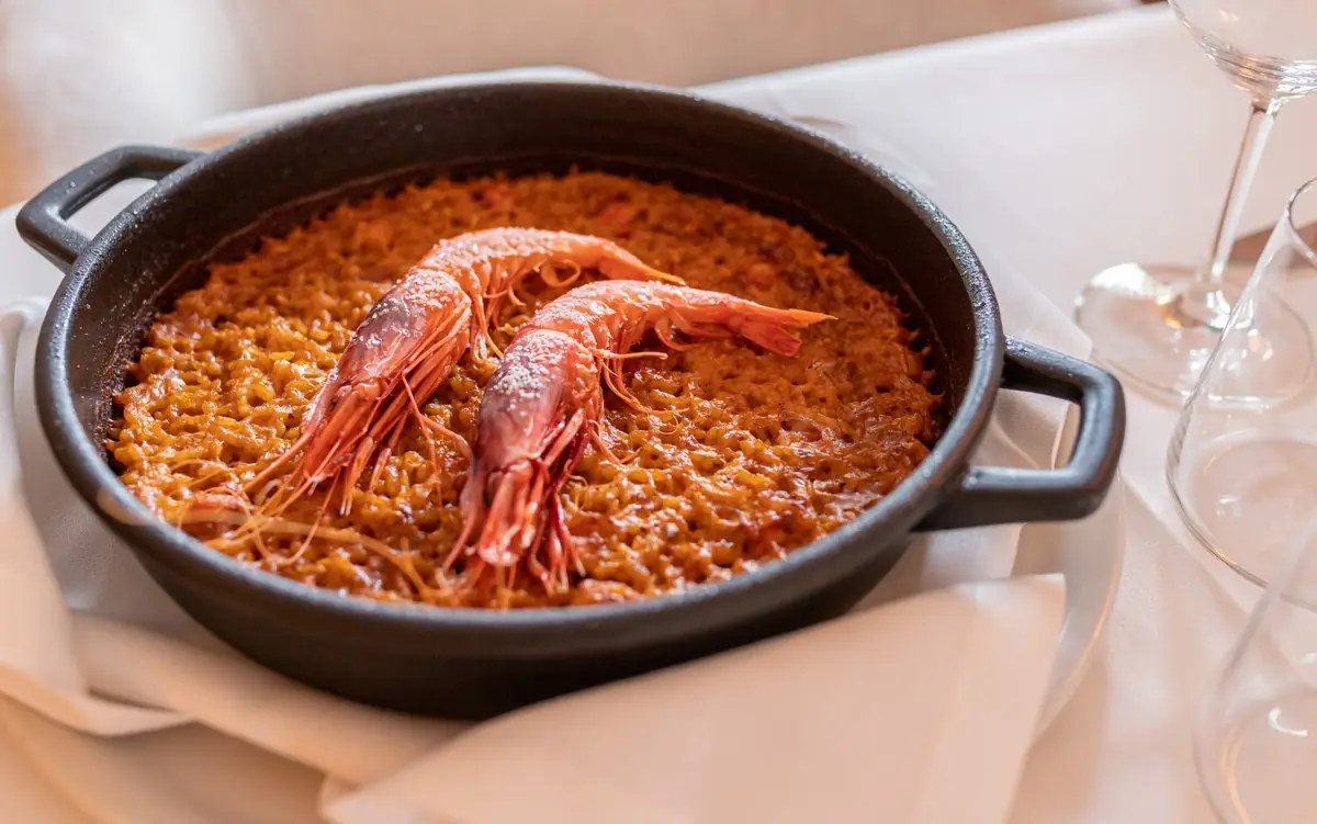 Seafood rice with two whole prawns on top, served in a black pan.
